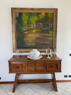 A wooden dresser with a painting of a bridge over water, a vase, and a lamp. - Apartment 'Villa Gabri 25 Wellness' with Wi-Fi and air conditioning (Seriate)