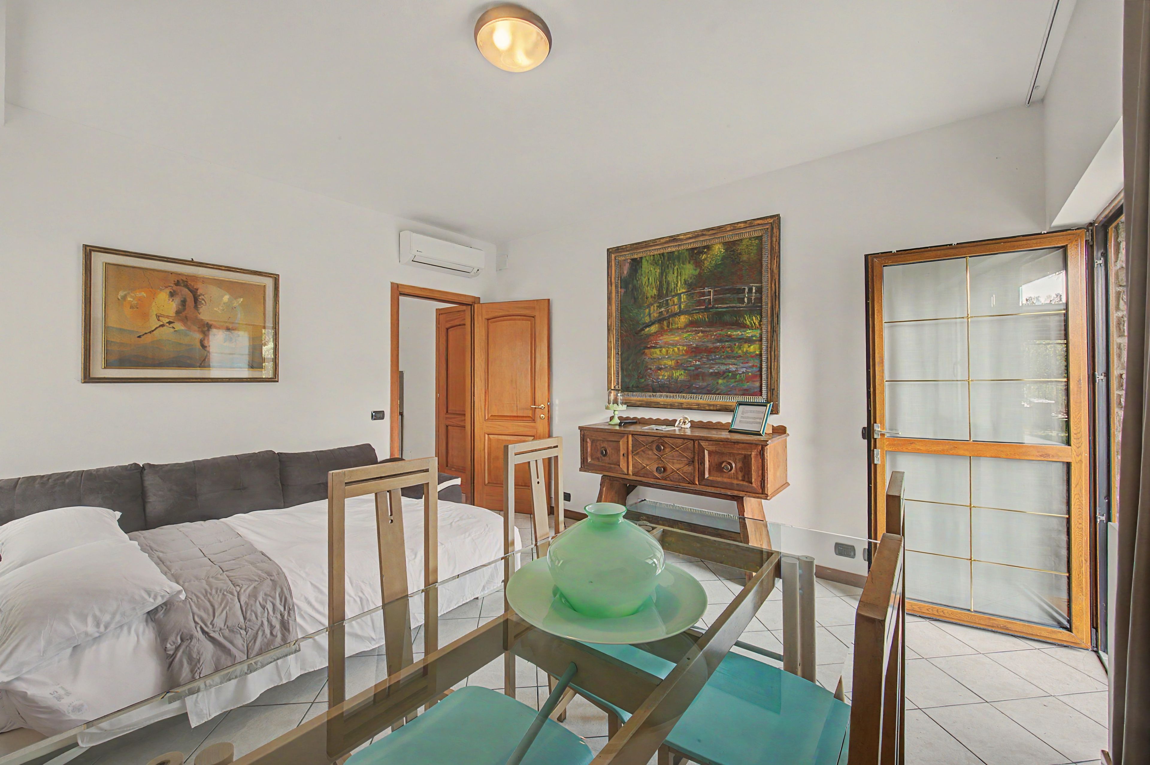 Un dormitorio con cama, cómoda, un cuadro y una puerta que da a otra habitación.