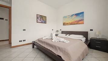 Habitación de hotel con cama, mesita de noche, lámpara, un cuadro y aire acondicionado instalado en la pared.