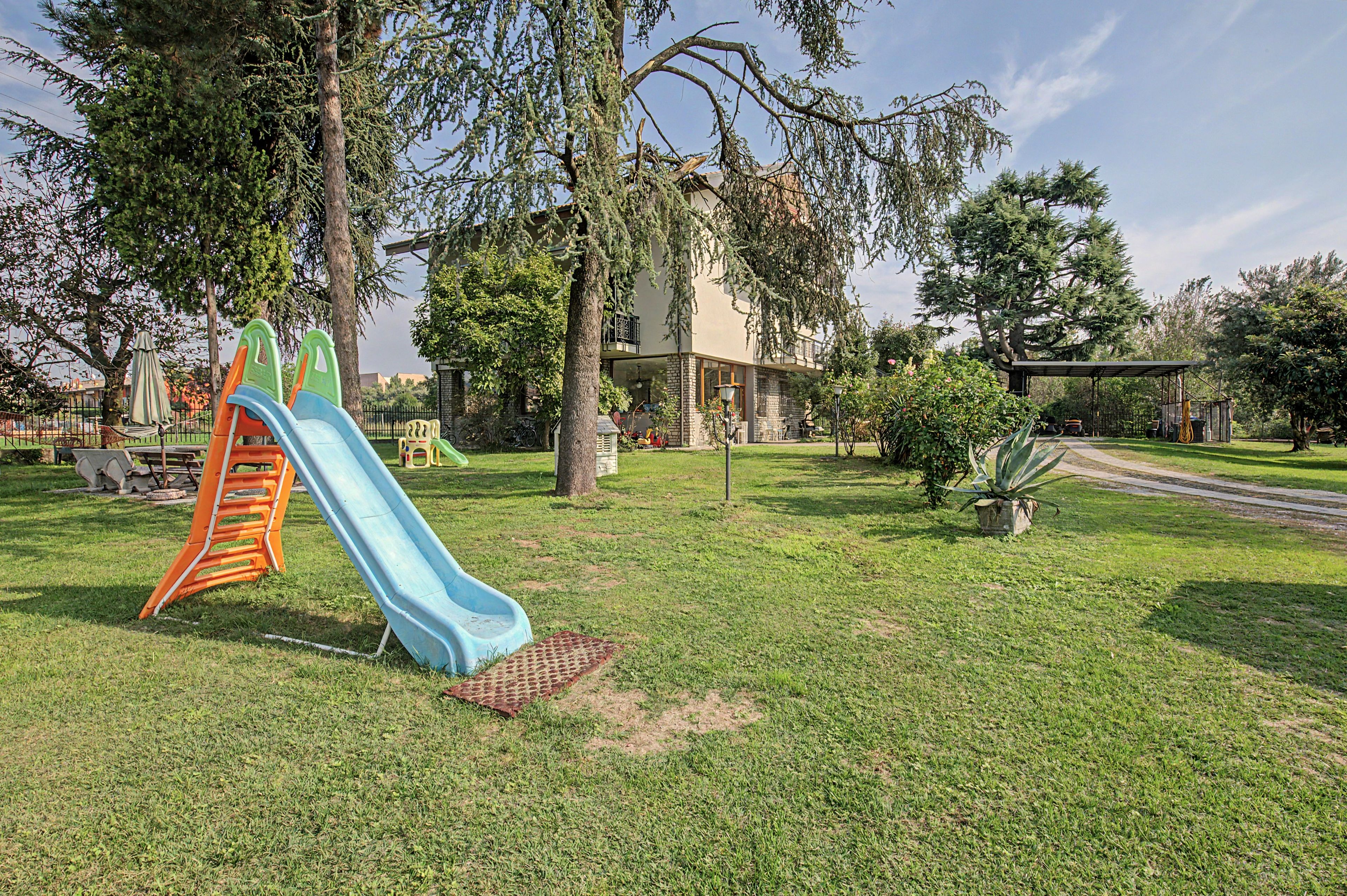 Ein Spielplatz mit Rutsche und Klettergerüst, umgeben von Gras und Bäumen.