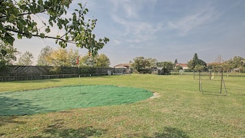 Un espacio al aire libre con césped artificial verde, un conjunto de columpios metálicos y una cerca de metal.