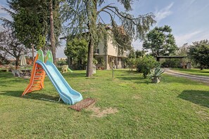 Un parque infantil con tobogán y estructura de escalada, rodeado de césped y árboles.