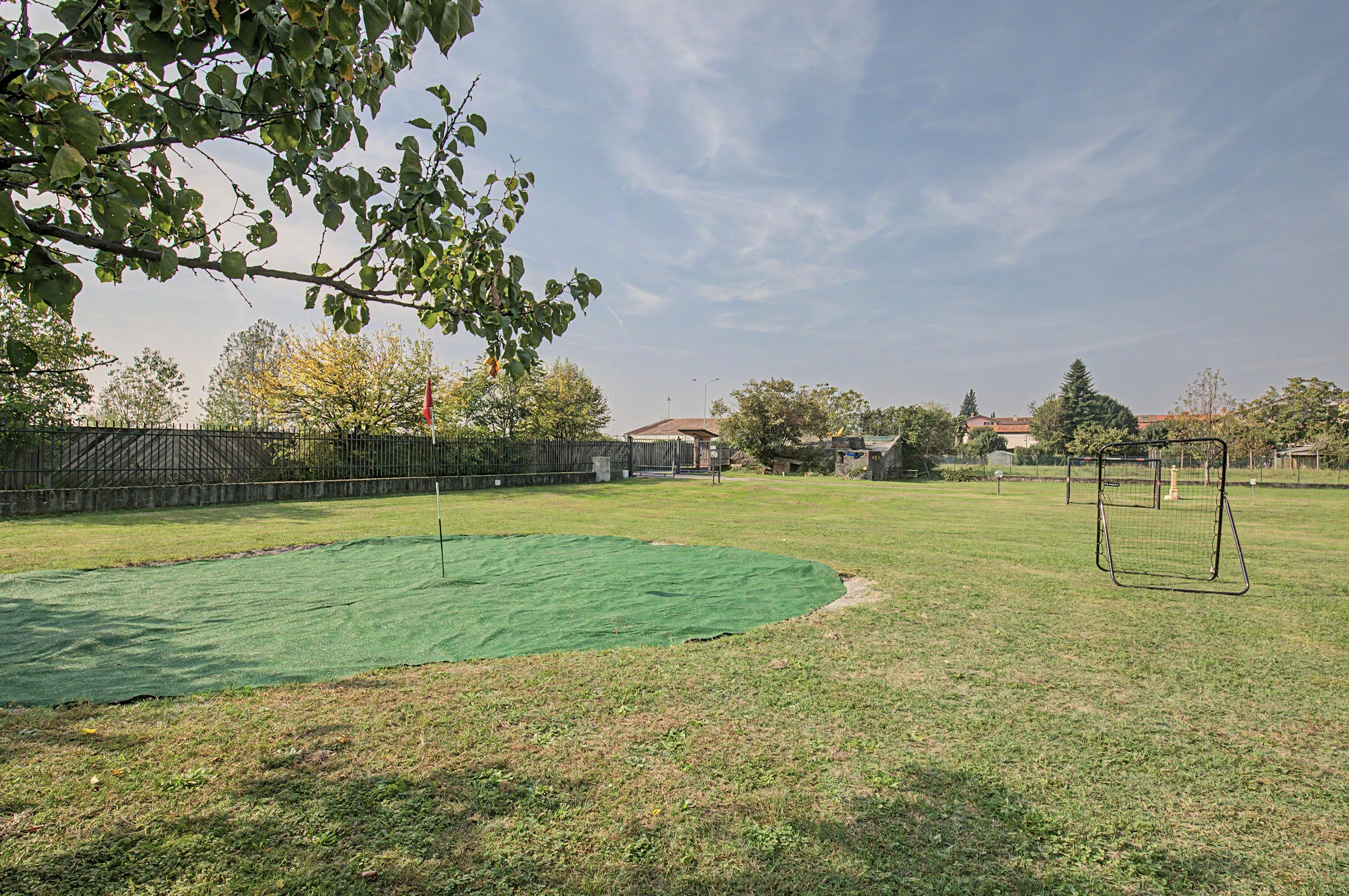 Zona exterior amb gespa artificial verda, un parc infantil de metall i una tanca de metall.