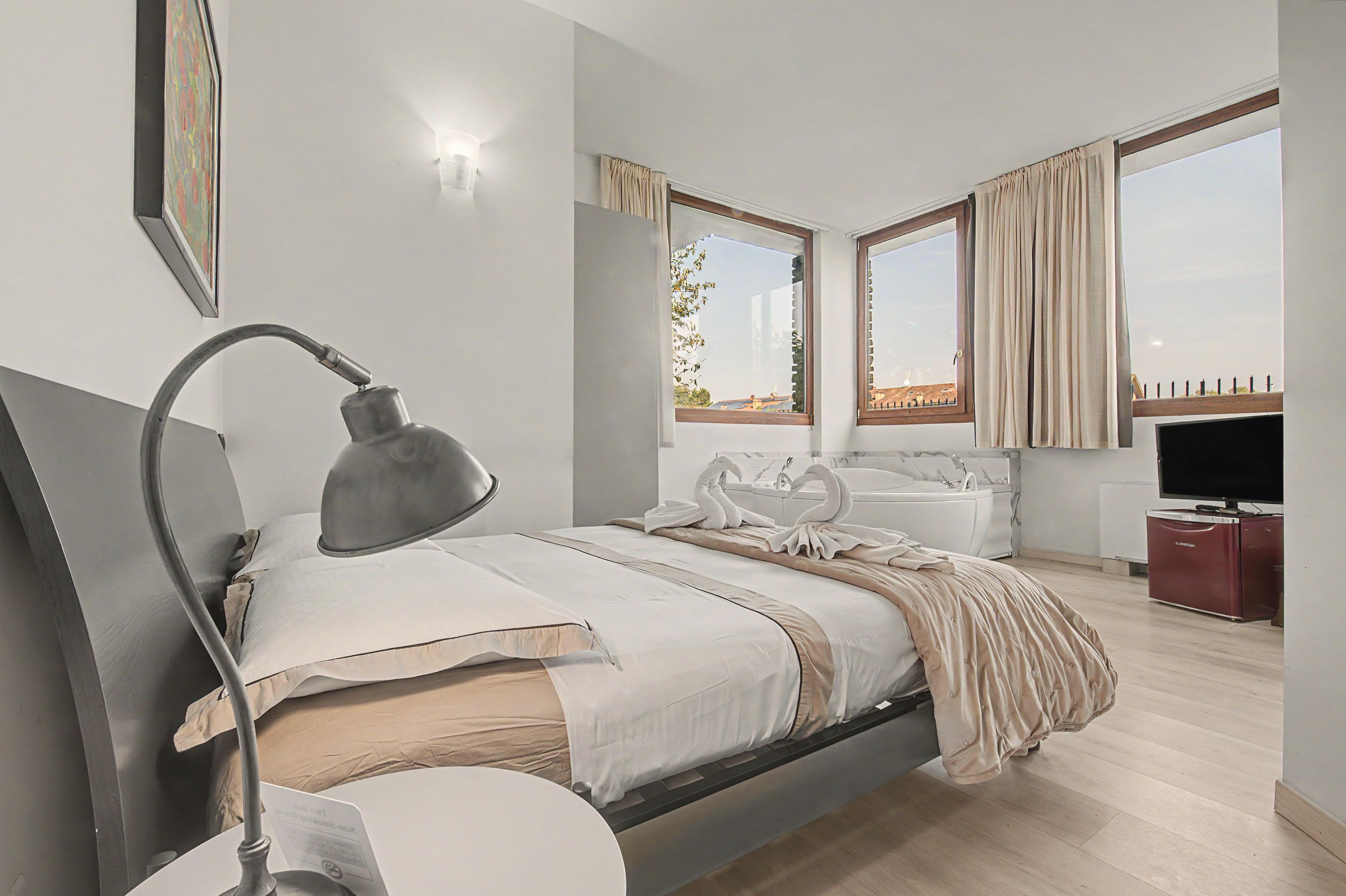 Ein modernes Schlafzimmer mit einem Bett, einer Nachttischlampe und Blick ins Freie durch große Fenster.