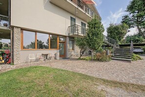 Un edificio con fachada de piedra, grandes ventanales, mesas al aire libre y una escalera que lleva a un nivel superior.