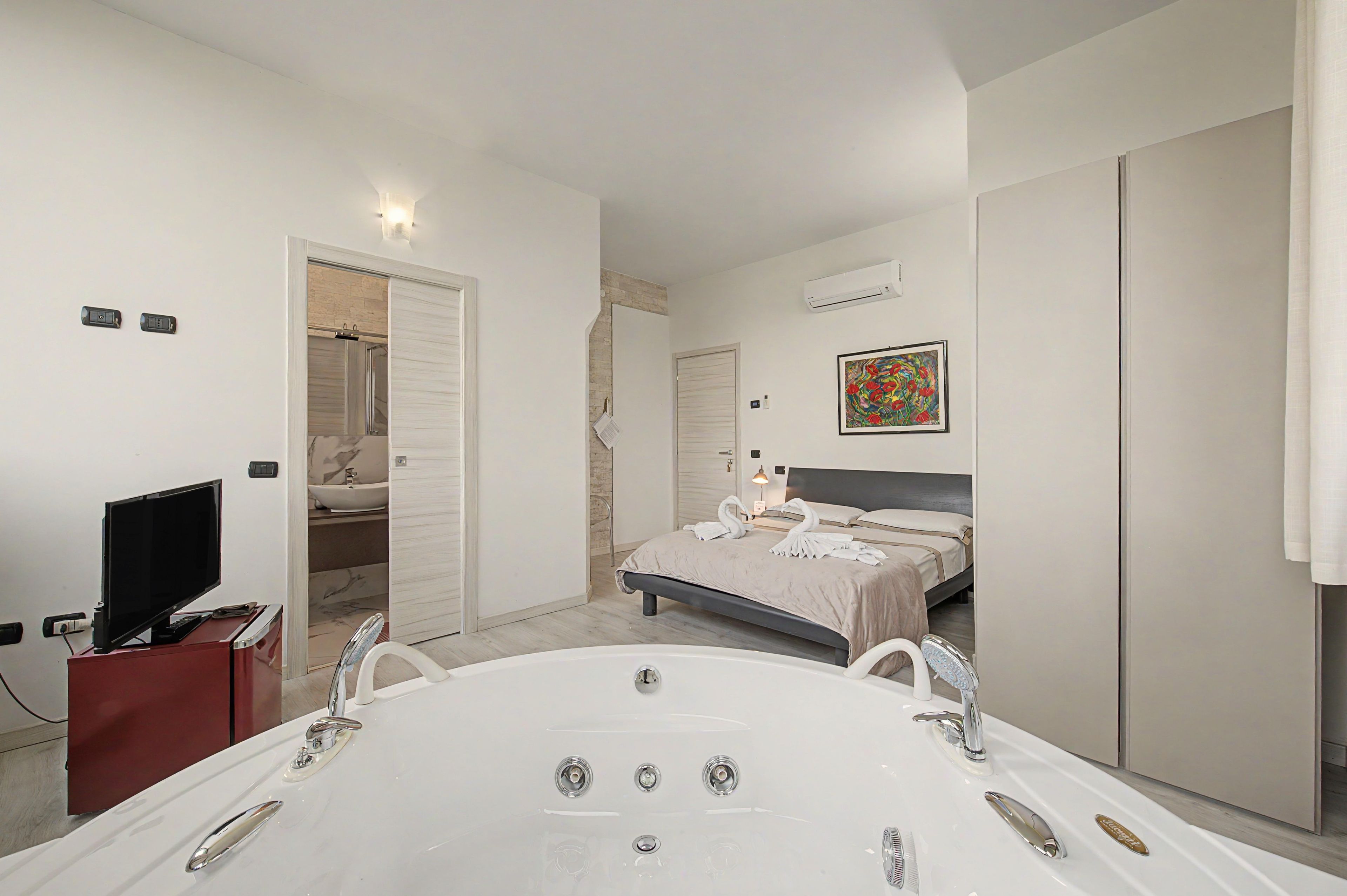 Ein modernes Schlafzimmer mit einem großen Bett, einem separaten Badezimmer mit Badewanne und einem Fernseher in der Ecke.