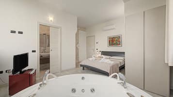Ein modernes Schlafzimmer mit einem großen Bett, einem separaten Badezimmer mit Badewanne und einem Fernseher in der Ecke.
