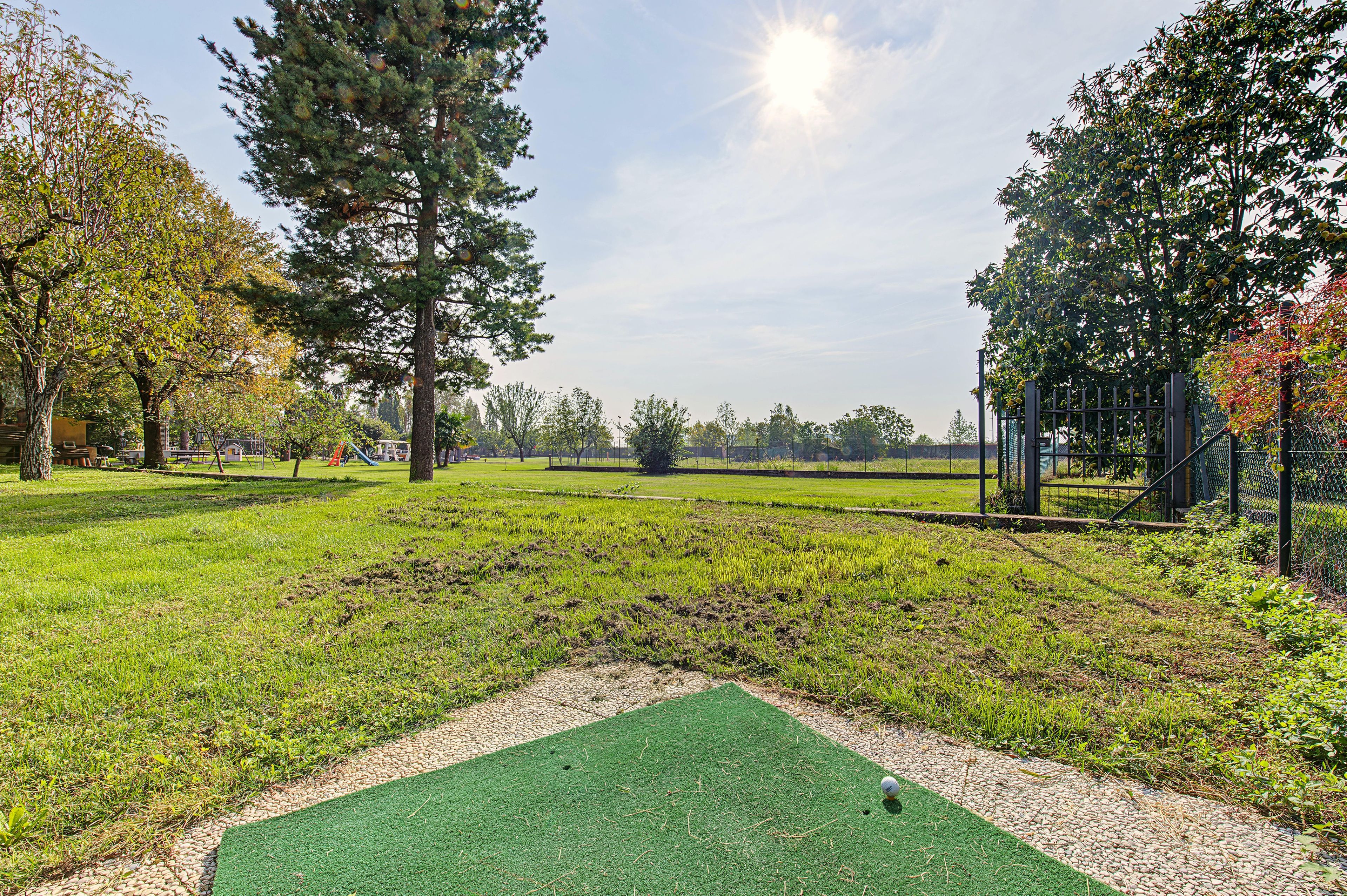 Un parcours de golf avec un green d’entraînement, des arbres et un ciel dégagé.