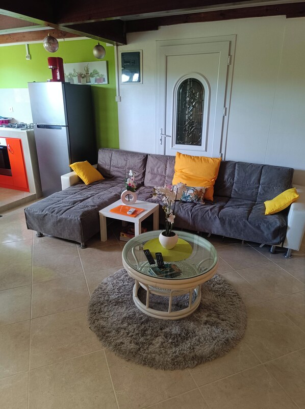 A living room with a sofa, a glass coffee table, and a kitchen area in the background. - T -SYSSY LODGE  FOR 2 ADULTS (WITHOUT CHILDREN) TO DISCOVER MARTINIQUE (Fort-de-France)