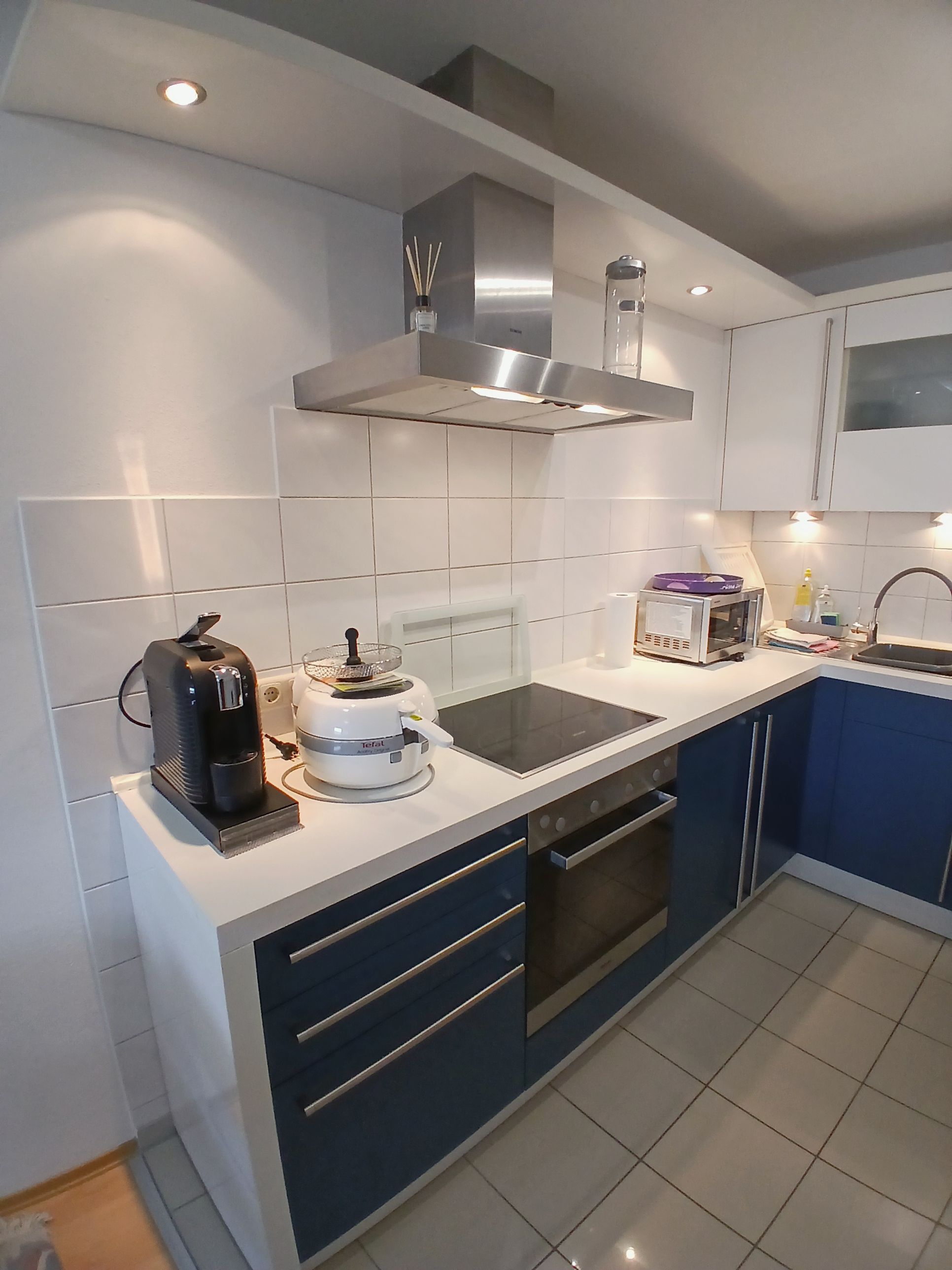 A modern kitchen with white cabinets, a stainless steel range hood, a coffee maker, a rice cooker, and a toaster.