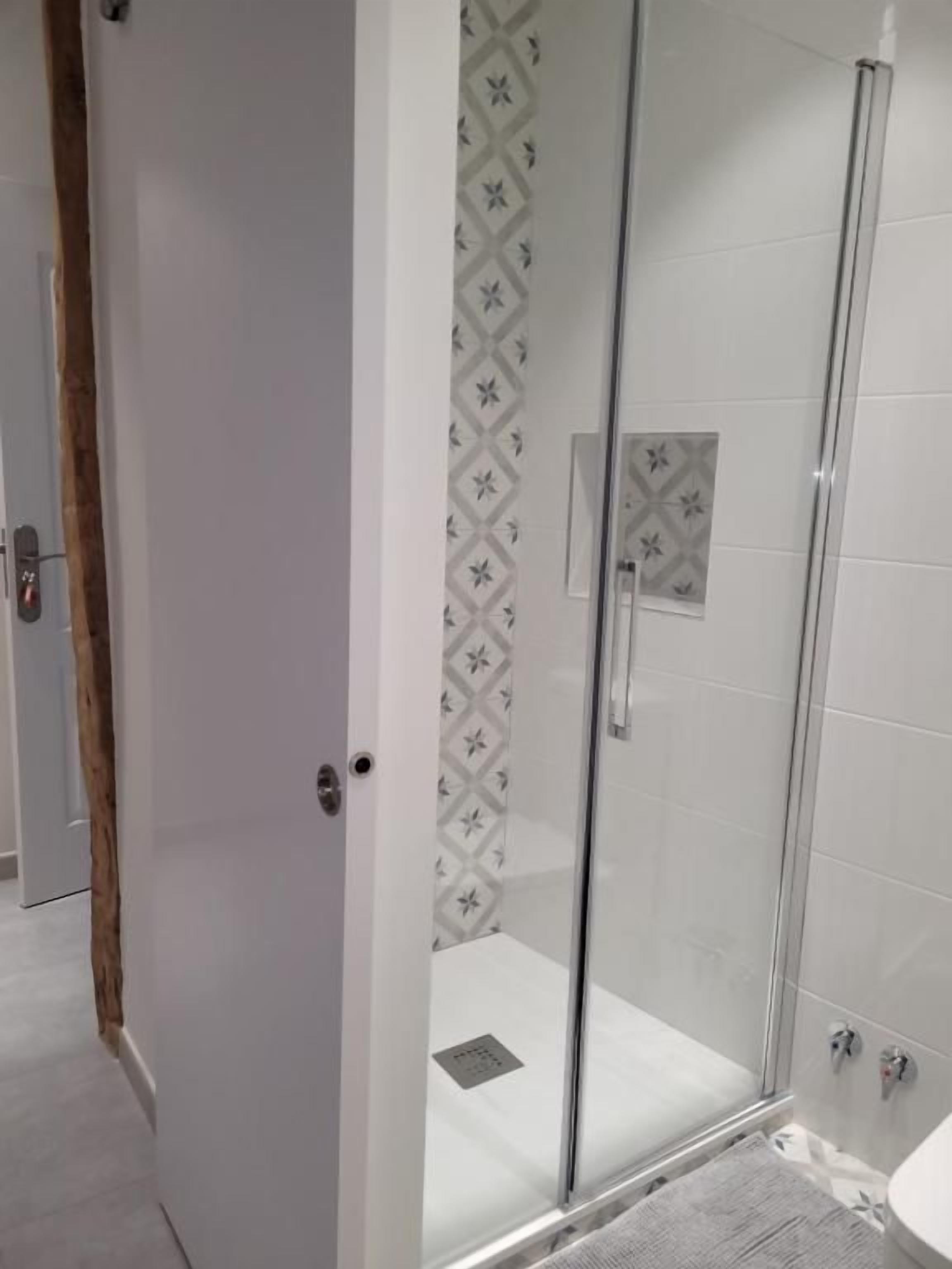 A glass-enclosed shower with a patterned wall and a visible drain.