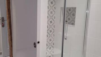 A glass-enclosed shower with a patterned wall and a visible drain.
