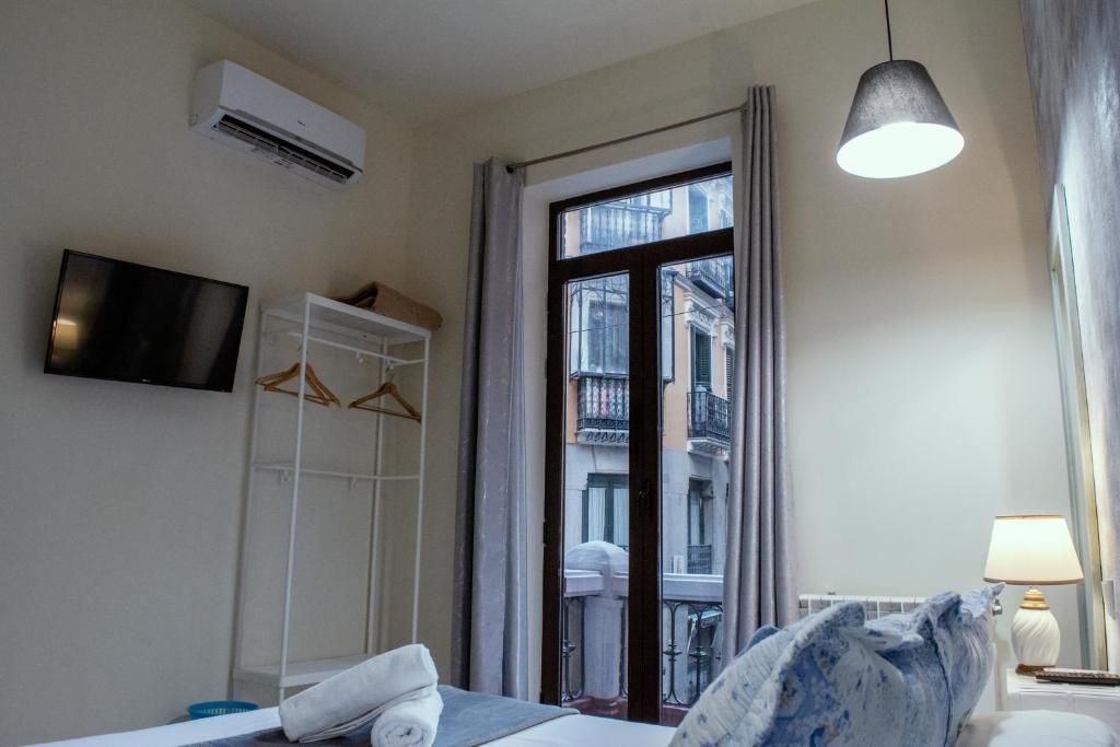 Habitación de hotel con cama, televisión, armario, ventana con vista a edificios y lámpara colgante.