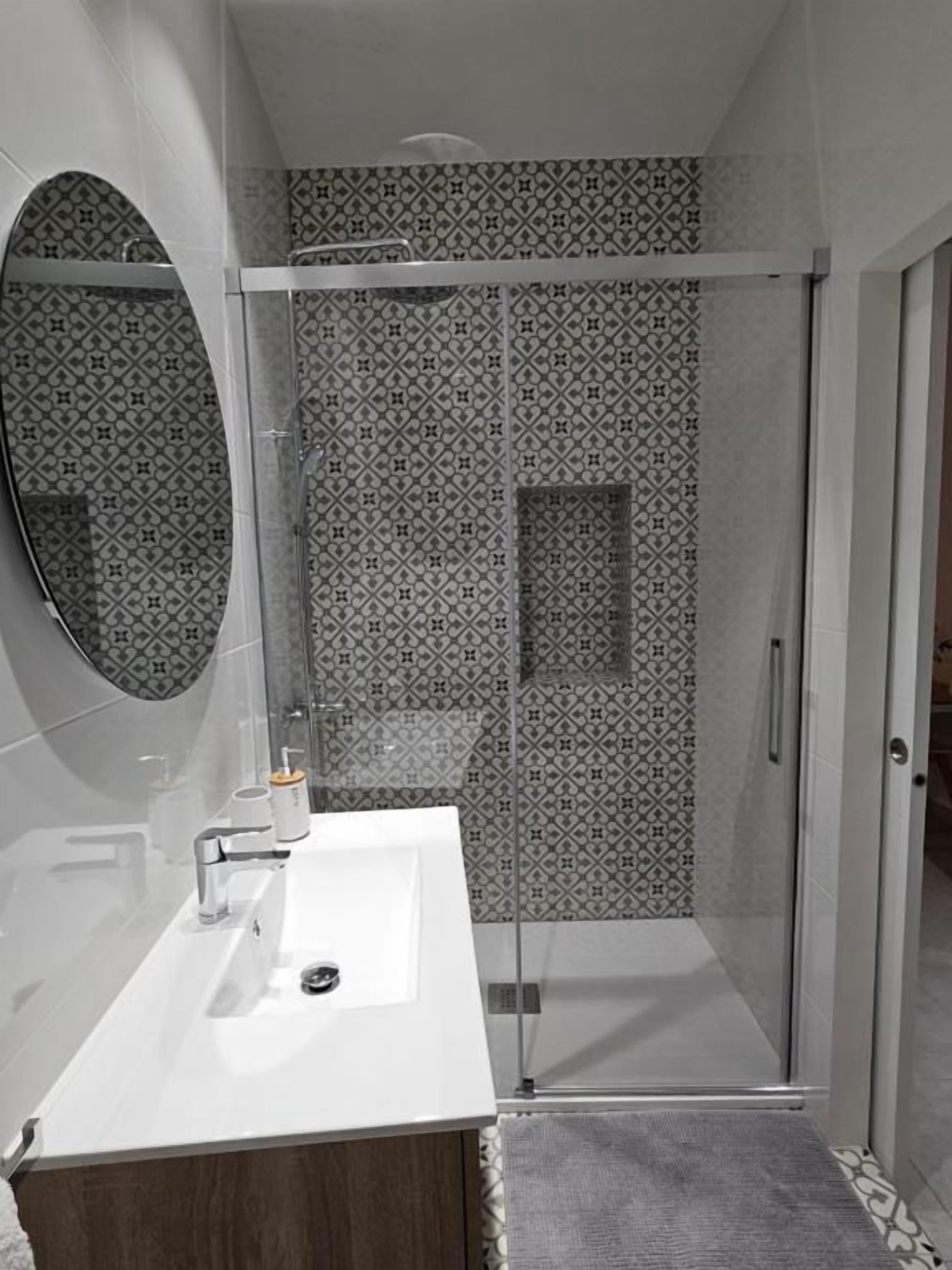 Un baño moderno con un lavamanos blanco, un espejo grande y una cabina de ducha.
