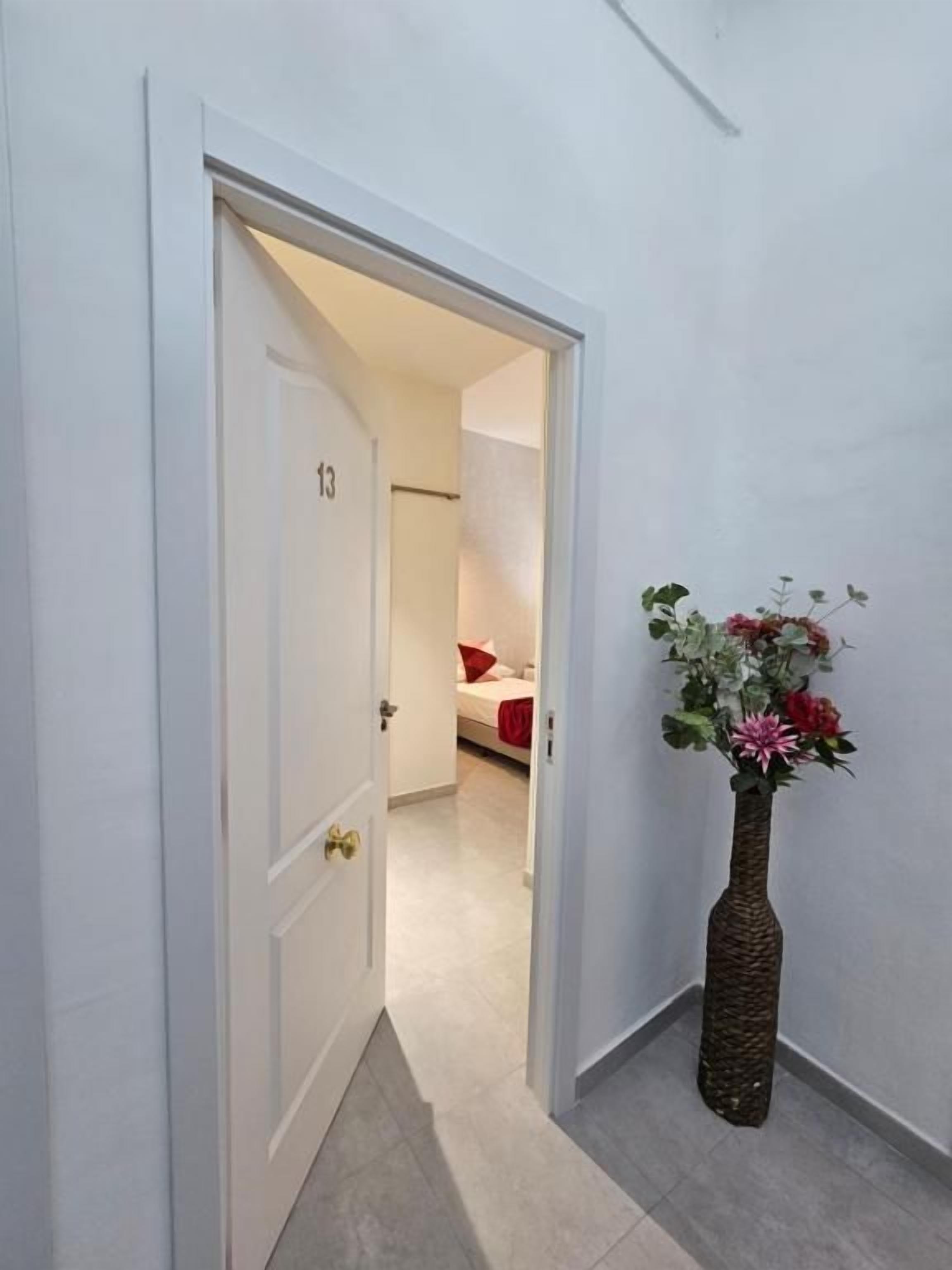 Un pasillo con una puerta que da a un dormitorio, un florero con flores y un suelo de baldosas.