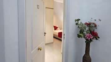 Un pasillo con una puerta que da a un dormitorio, un florero con flores y un suelo de baldosas.