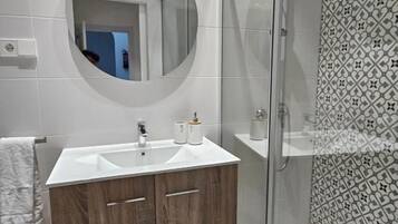 Een moderne badkamer met een houten wastafelmeubel, een ronde spiegel en een douchegedeelte met een betegelde vloer.