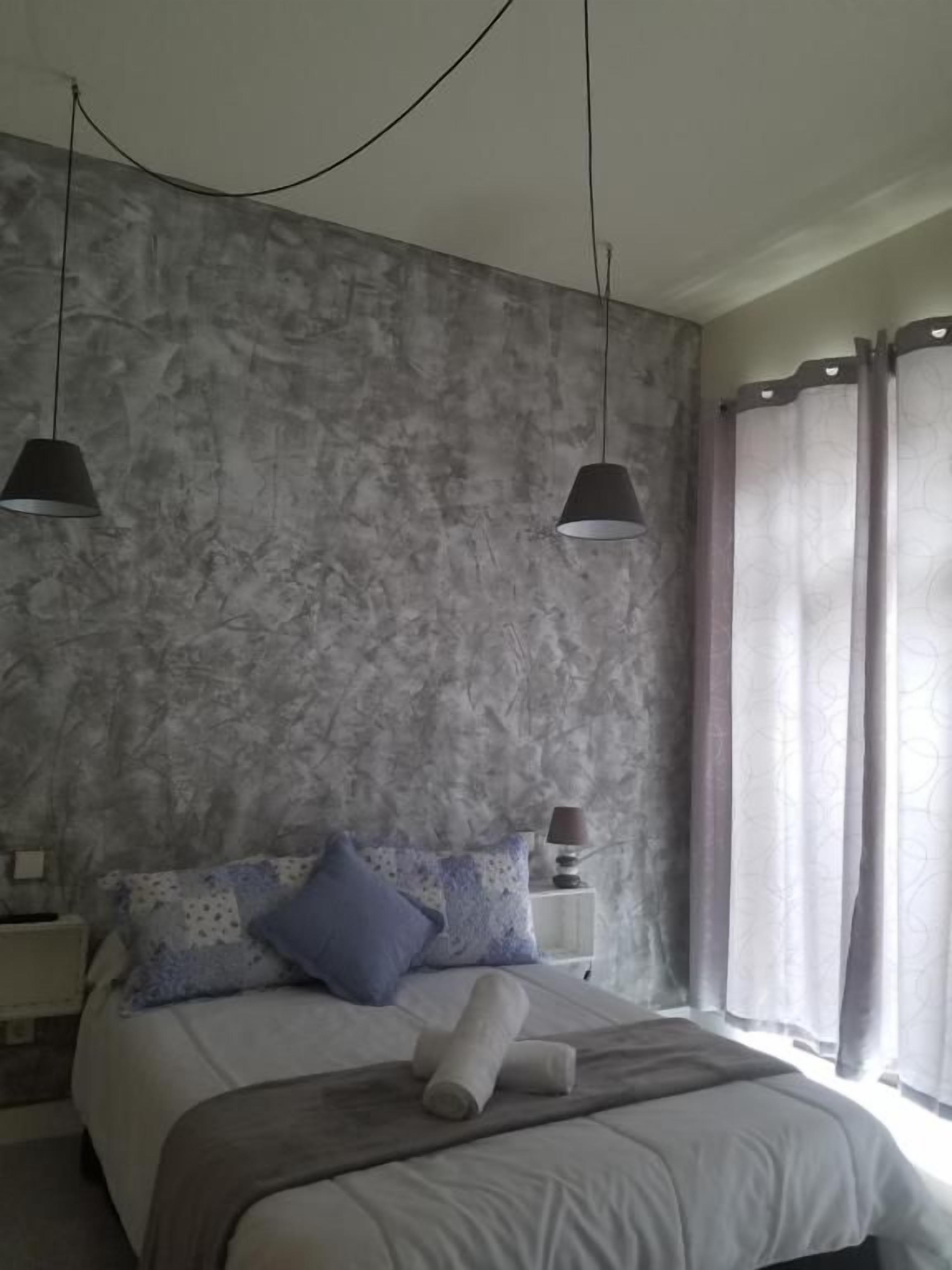 Un dormitorio con cama, mesitas de noche y una ventana con cortinas.