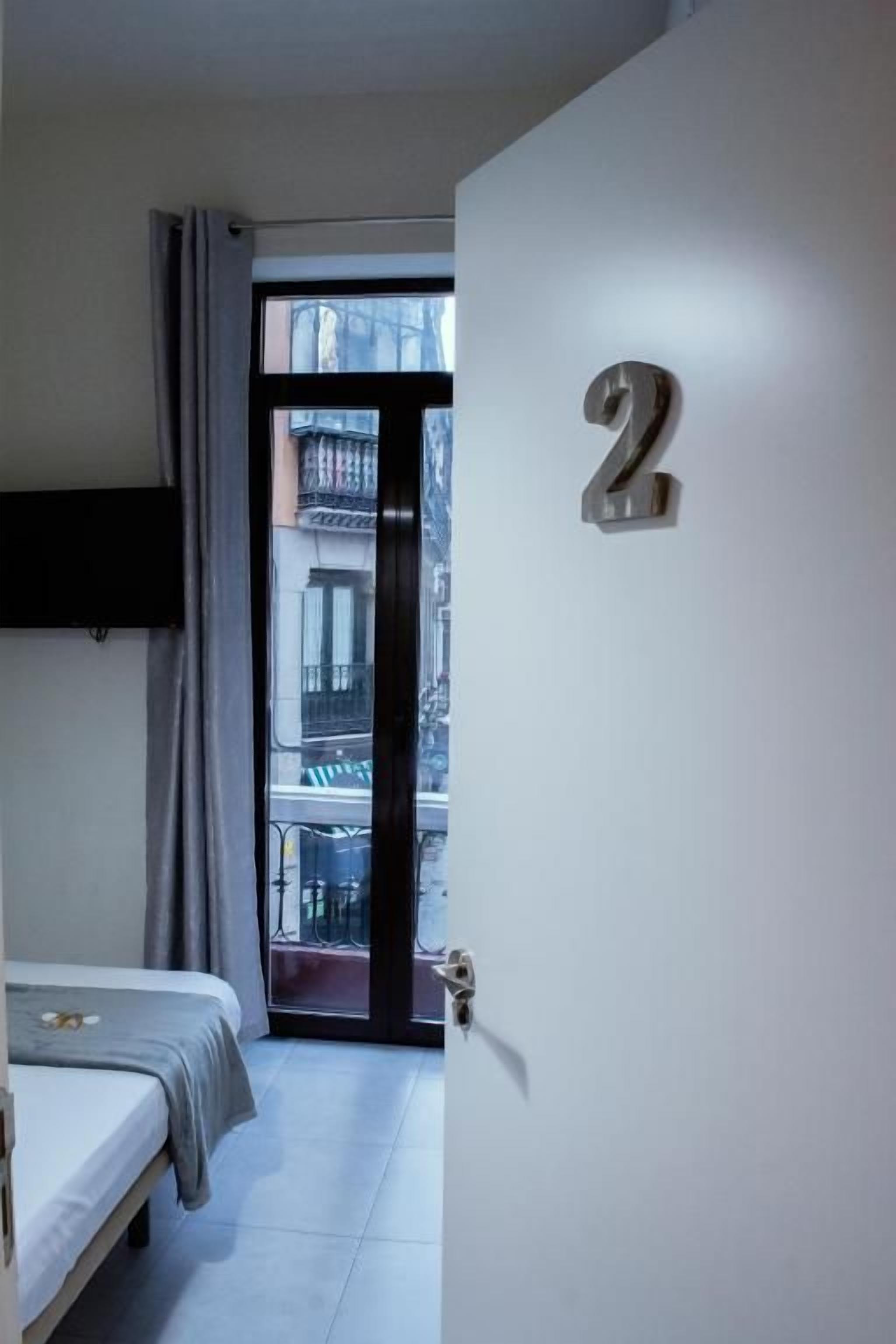 Une chambre avec un lit, une porte portant un numéro et une vue sur l’extérieur.