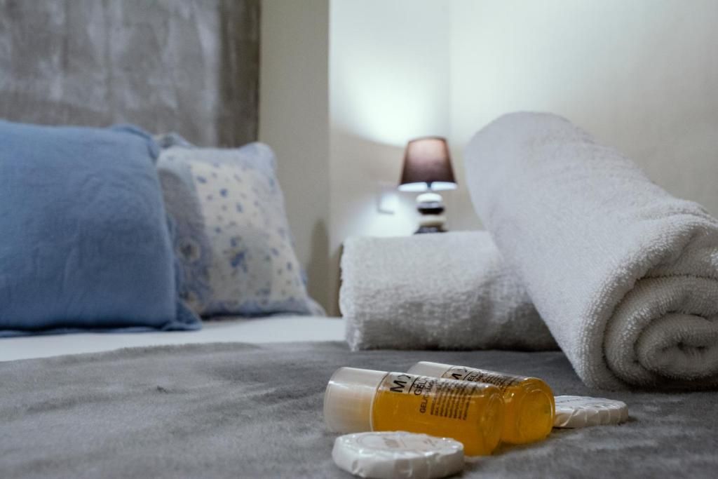 Una cama con una toalla blanca enrollada, una botella de medicamentos y un organizador de pastillas sobre una manta gris.