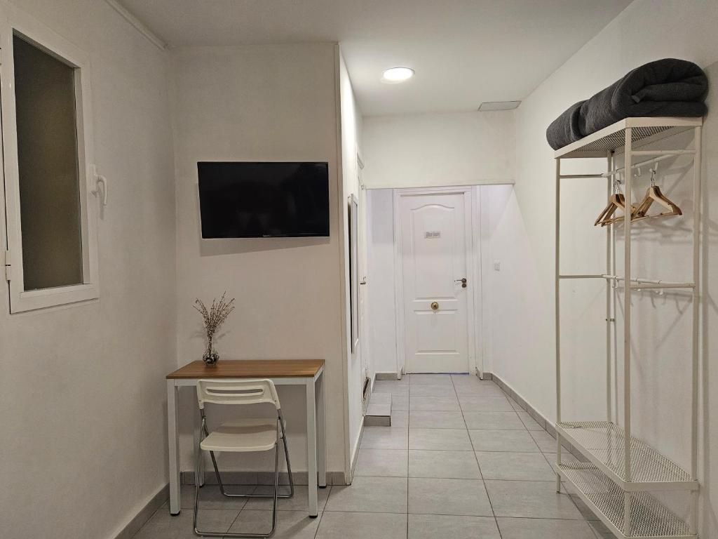 A narrow hallway with a white door at the end, a small table with a chair, and a TV mounted on the wall.