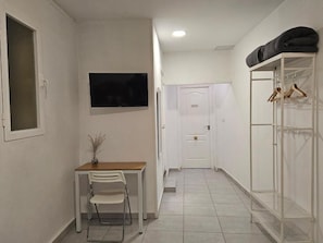 A narrow hallway with a white door at the end, a small table with a chair, and a TV mounted on the wall. - Casa Lemus (Madrid)