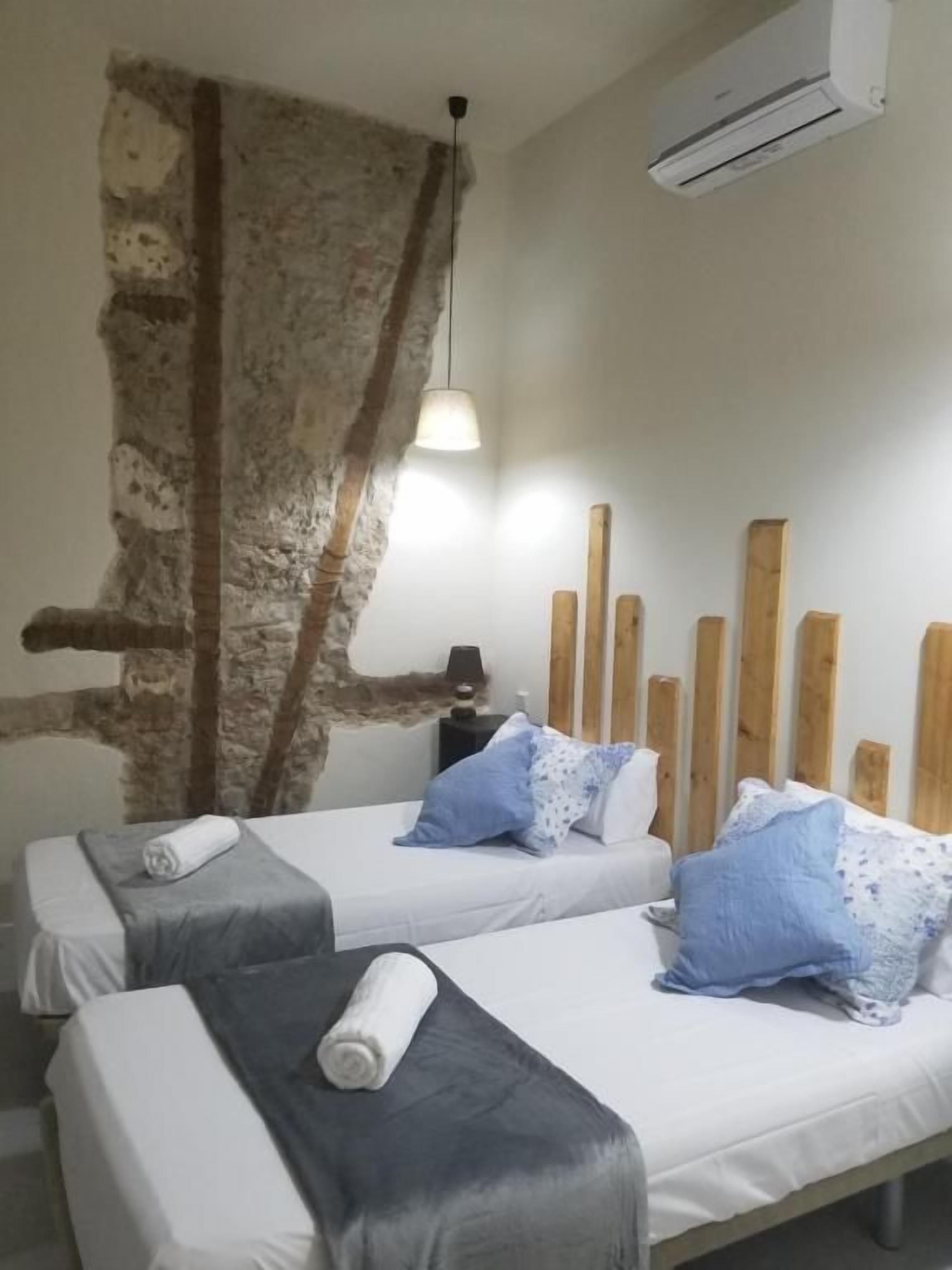Una habitación con dos camas, pared de piedra, cabecero de madera y un equipo de aire acondicionado.