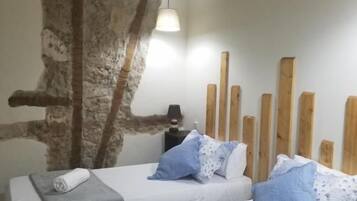 Una habitación con dos camas, pared de piedra, cabecero de madera y un equipo de aire acondicionado.