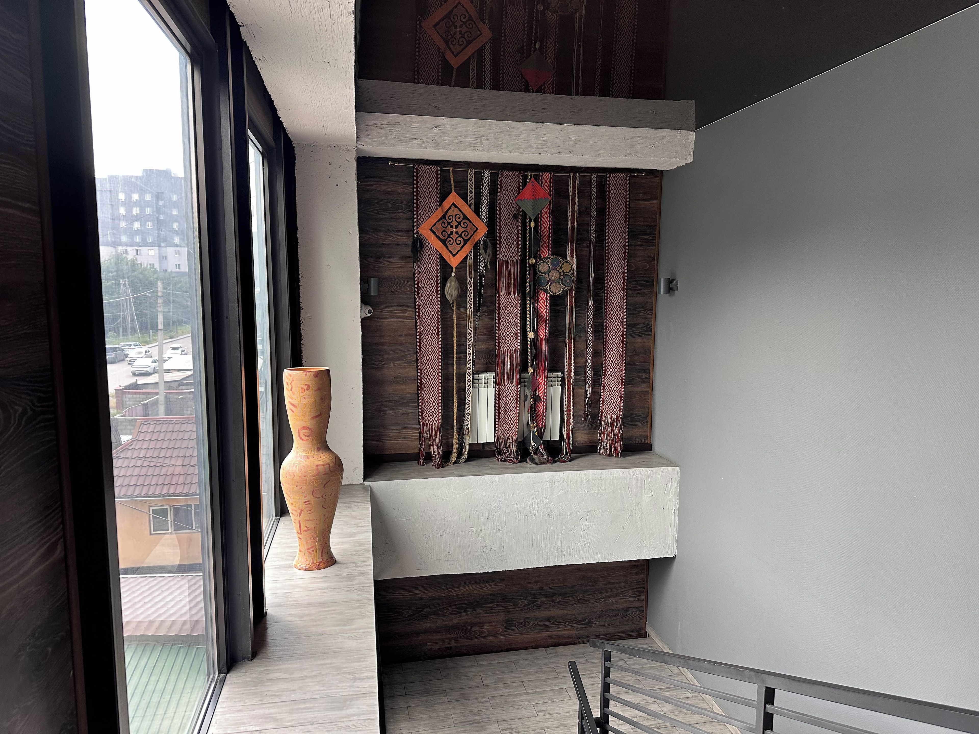 Un intérieur moderne avec une grande fenêtre, un vase décoratif et une étagère murale agrémentée de textiles à motifs.