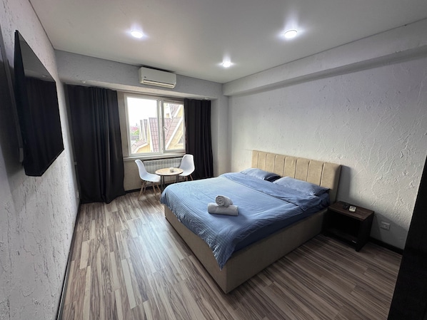 A hotel room with a bed, a small table with two chairs, a window, and an air conditioning unit. - Gatsby Vostok 5 (Bishkek)