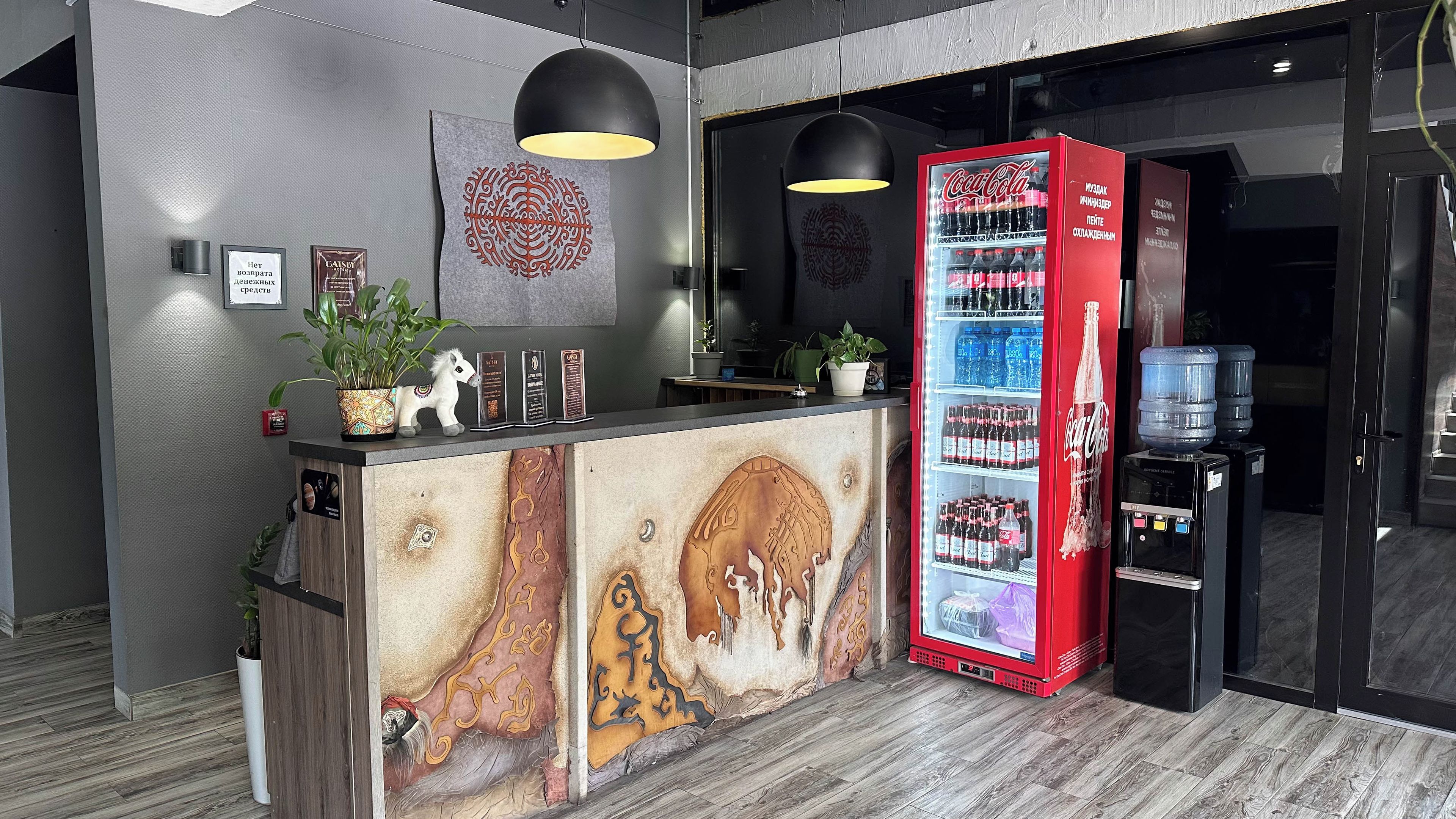 Un comptoir d’accueil agrémenté d’une fresque décorative, un réfrigérateur Coca-Cola et un distributeur d’eau.