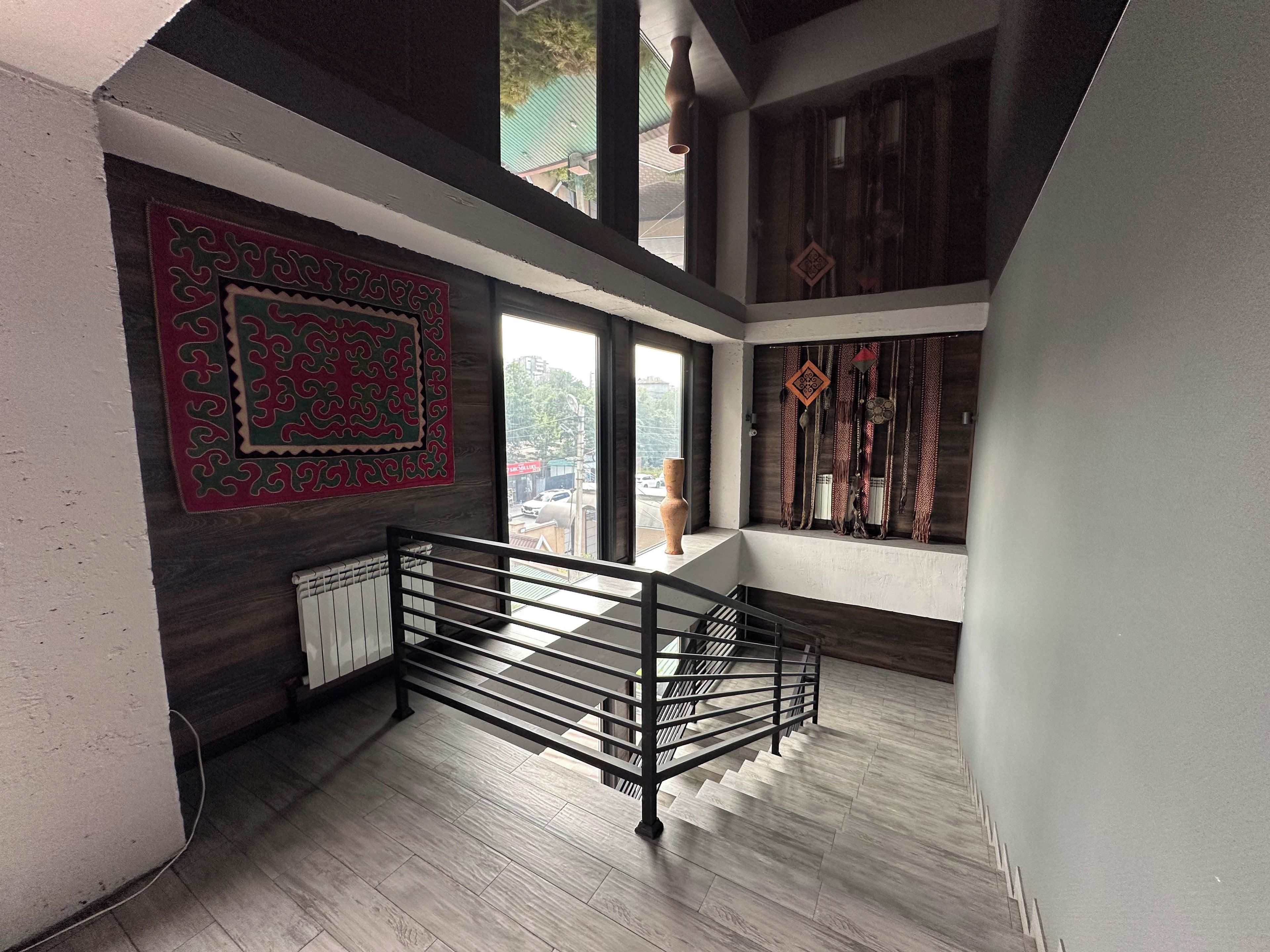 Un interior moderno con una escalera, un tapiz con estampado y vistas a través de una ventana.