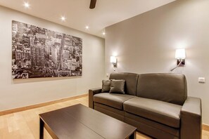 A modern living room with a large black and white cityscape painting, a leather sofa, two wall-mounted lamps, and a dark wooden coffee table. - Opera Bastille - Elegant Studio (Paris)