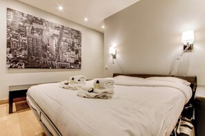 A hotel room with a large bed, a cityscape painting on the wall, and two wall-mounted lamps. - Opera Bastille - Elegant Studio (Paris)