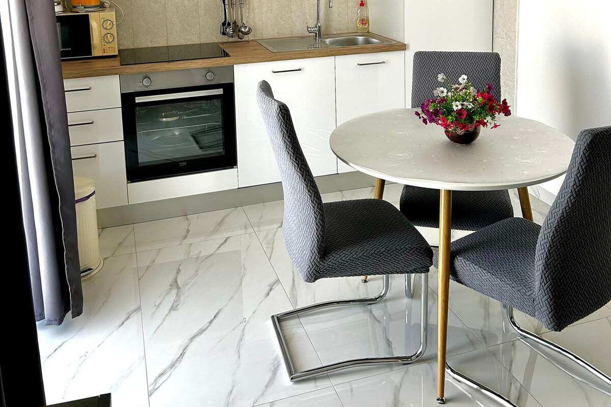 A modern kitchen with a built-in oven, a dining table with chairs, and a flower vase.