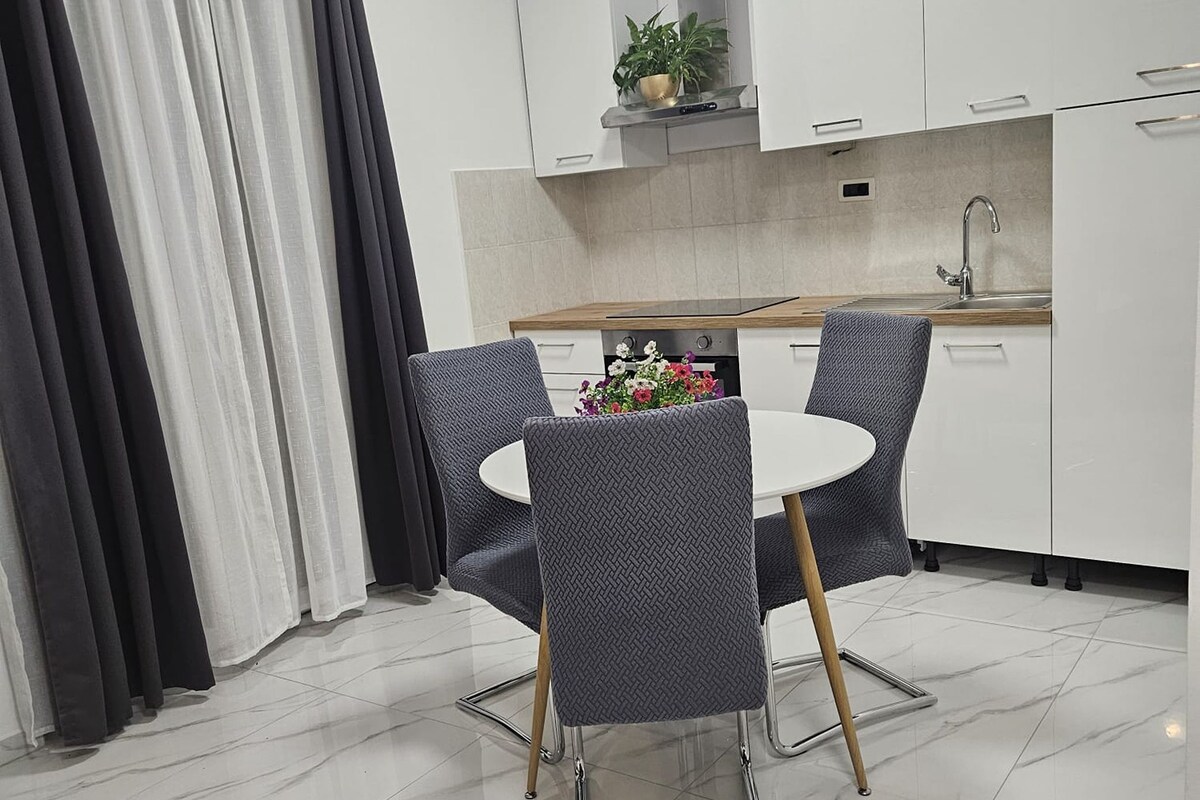 A modern kitchen with white cabinets, a stainless steel sink, and a round dining table with two chairs.
