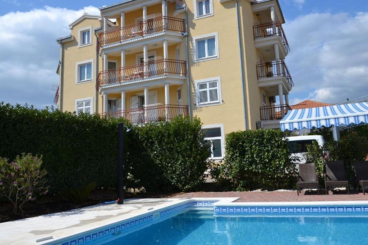 A multi-story hotel with balconies, a swimming pool, and a covered outdoor seating area.