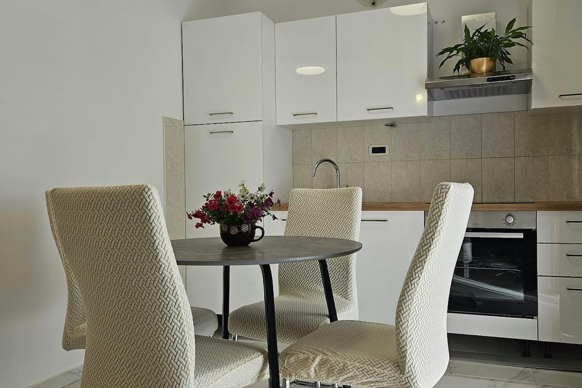 A modern kitchen with white cabinets, a stainless steel oven, and a dining area with a round table and woven chairs.