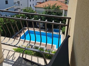 A balcony with a view of a swimming pool, surrounded by greenery and buildings. - Mary Apartments & Pool (Trogir)