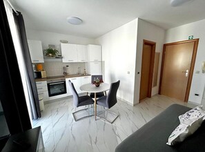 Habitación de hotel compacta con kitchenette, comedor con mesa y sillas, y una cama.