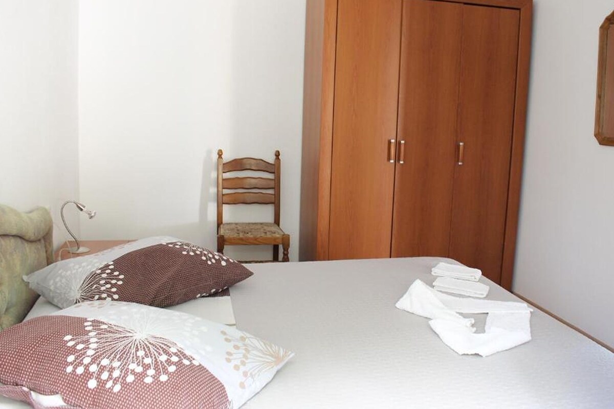 A bedroom with a bed, pillows, a wooden wardrobe, and a chair.