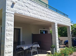 A covered outdoor seating area with a table and chairs, a potted plant, and a view of a blue car parked outside. - Apartments Anton & Blanka (Orebic)