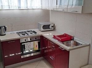 A compact kitchen with a gas stove, microwave, and a red dish rack. - Apartments Anton & Blanka (Orebic)