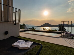 A balcony with a view of the sea and mountains during sunset.
