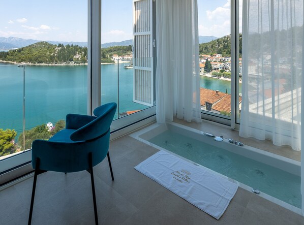 A room with a view of a lake, a blue chair, a small pool, and a white towel on the floor.