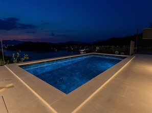 A rectangular swimming pool with clear blue water, surrounded by a concrete deck.