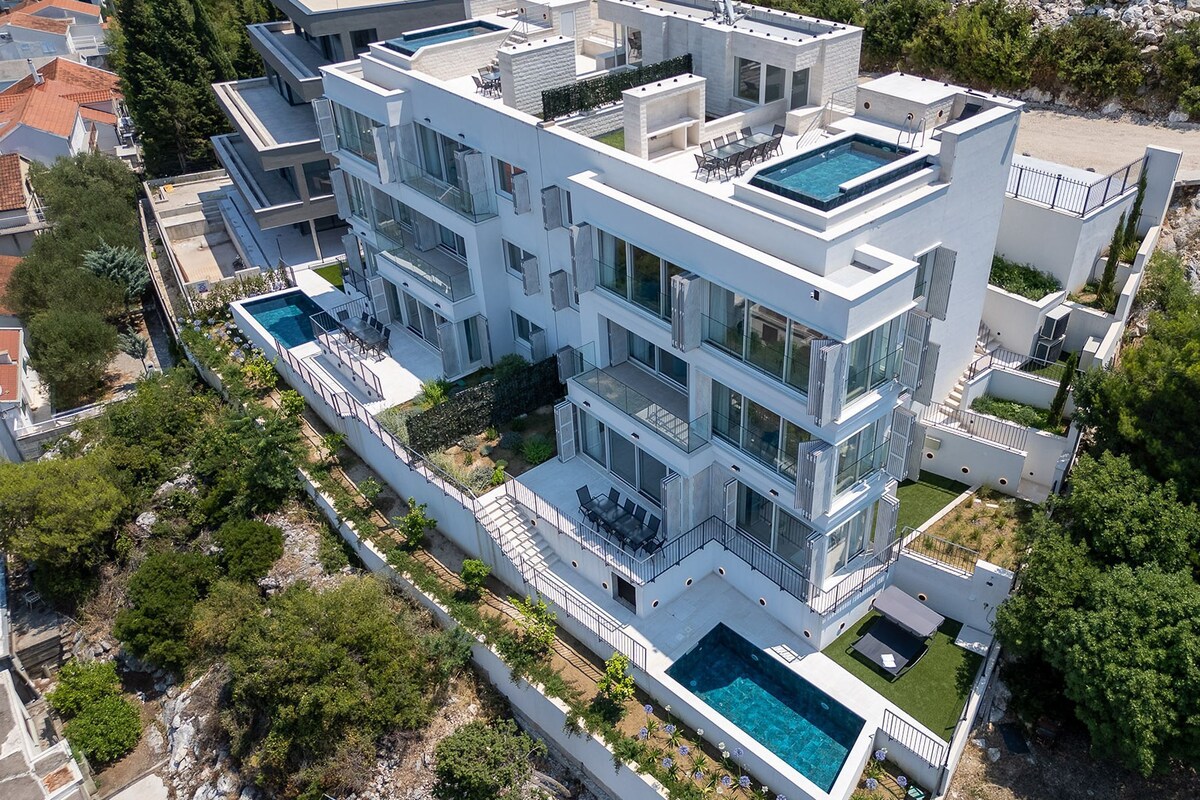 A modern multi-story building with a rooftop pool, balconies, and a landscaped garden.