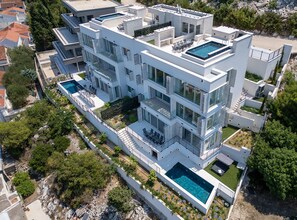 A modern multi-story building with a rooftop pool, balconies, and a landscaped garden.