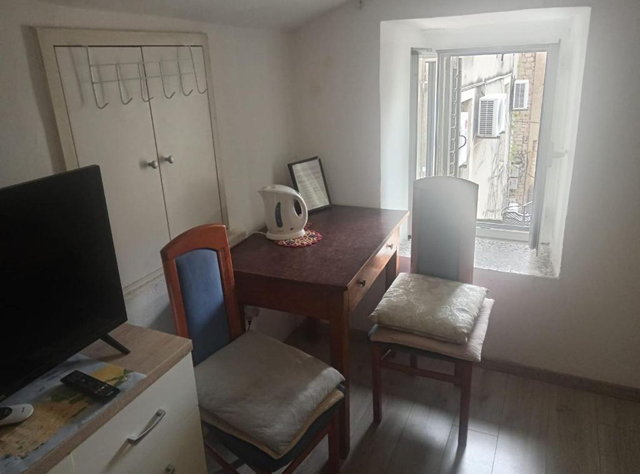 Uma pequena sala de jantar com uma mesa, cadeiras, chaleira e televisão.