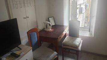 Uma pequena sala de jantar com uma mesa, cadeiras, chaleira e televisão.